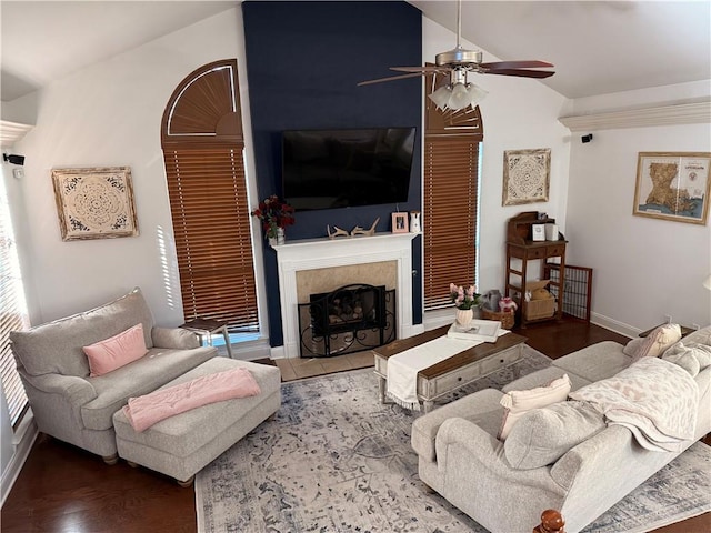 living room with baseboards, wood finished floors, a tiled fireplace, a ceiling fan, and lofted ceiling