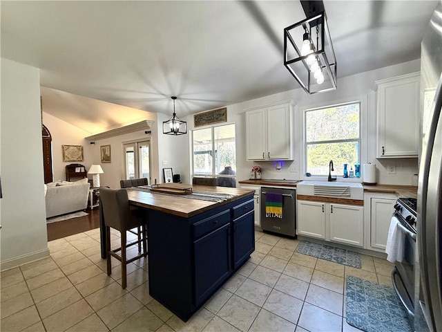 kitchen with butcher block counters, a sink, white cabinets, open floor plan, and appliances with stainless steel finishes