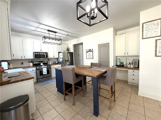 kitchen featuring light tile patterned flooring, butcher block counters, a sink, appliances with stainless steel finishes, and built in desk