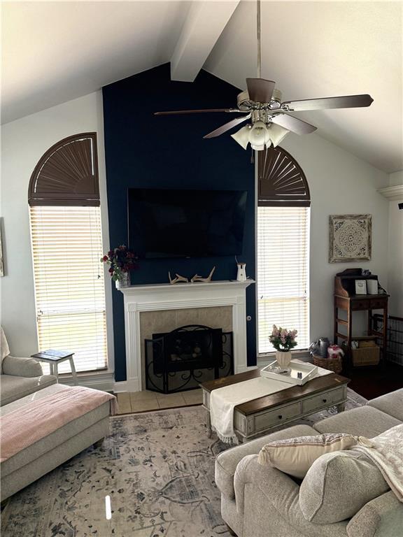 living area featuring a tiled fireplace, a ceiling fan, plenty of natural light, and vaulted ceiling with beams
