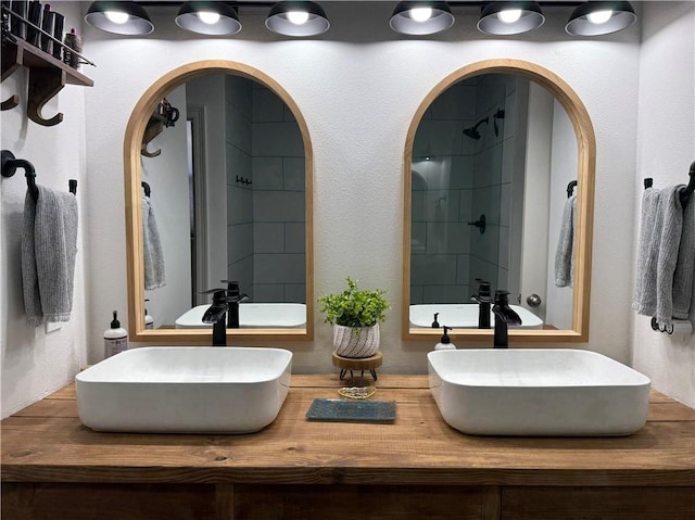 full bathroom with double vanity, tiled shower, and a sink