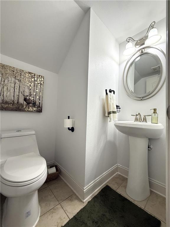 bathroom featuring baseboards, lofted ceiling, toilet, and tile patterned floors