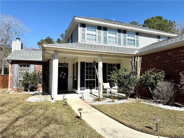 traditional home with a porch, a chimney, a front lawn, and brick siding