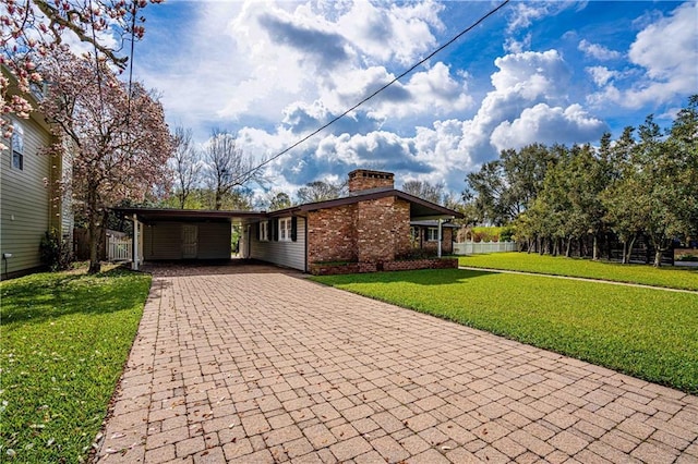 mid-century home with decorative driveway, brick siding, a chimney, fence, and a front lawn