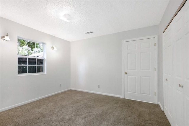 carpeted empty room with visible vents, a textured ceiling, and baseboards