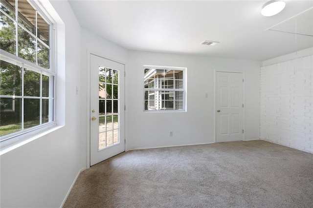 interior space featuring a healthy amount of sunlight, carpet flooring, visible vents, and brick wall