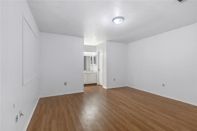 spare room with a textured ceiling, baseboards, and wood finished floors