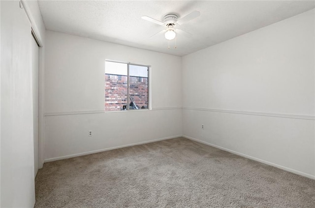 empty room with ceiling fan, a textured ceiling, carpet, and baseboards