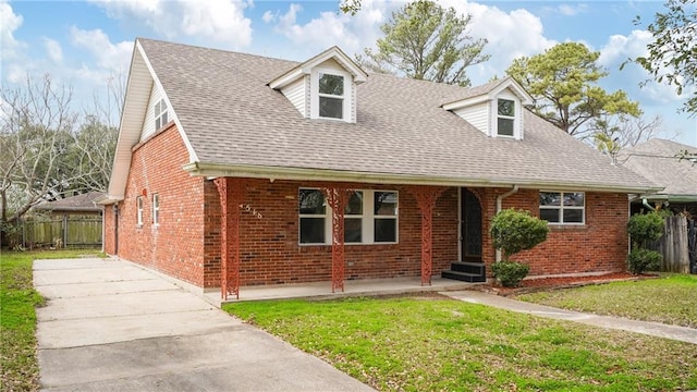 new england style home featuring brick siding, roof with shingles, a front yard, and fence