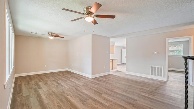 spare room with light wood-style floors, visible vents, a textured ceiling, and baseboards