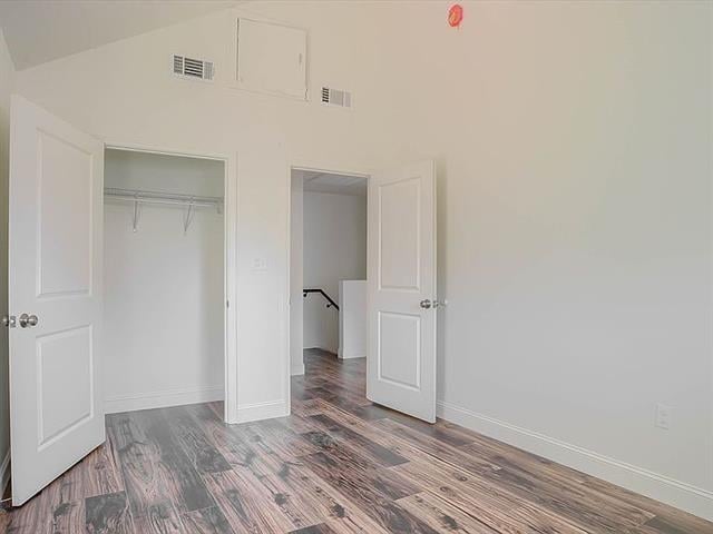 unfurnished bedroom featuring lofted ceiling, a closet, visible vents, wood finished floors, and baseboards