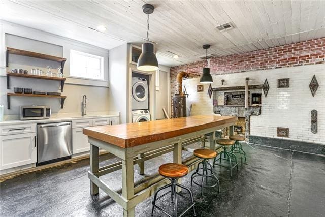 bar featuring stacked washer and clothes dryer, visible vents, appliances with stainless steel finishes, a sink, and brick wall