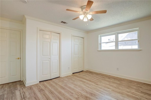 unfurnished bedroom with a textured ceiling, light wood-style flooring, visible vents, multiple closets, and ornamental molding