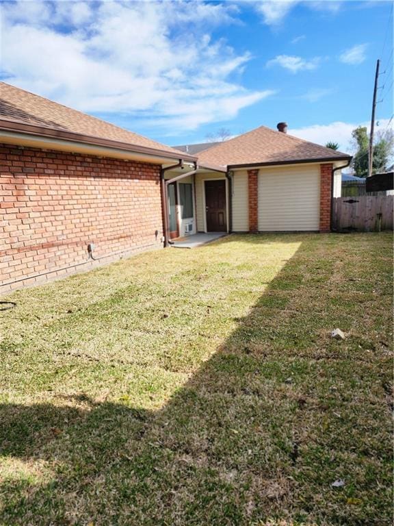 exterior space featuring brick siding, a shingled roof, fence, and a yard