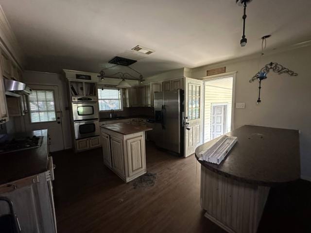 kitchen with stainless steel appliances, visible vents, ventilation hood, dark countertops, and dark wood finished floors