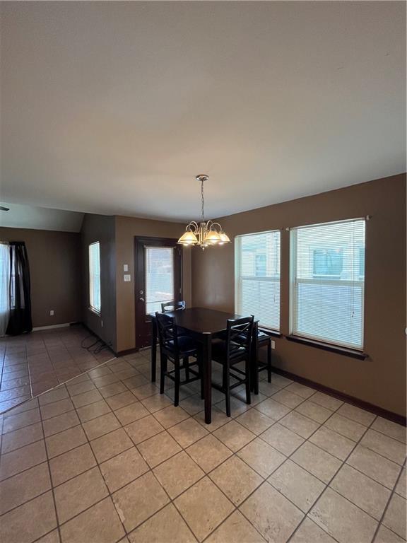 unfurnished dining area with light tile patterned floors, baseboards, and an inviting chandelier