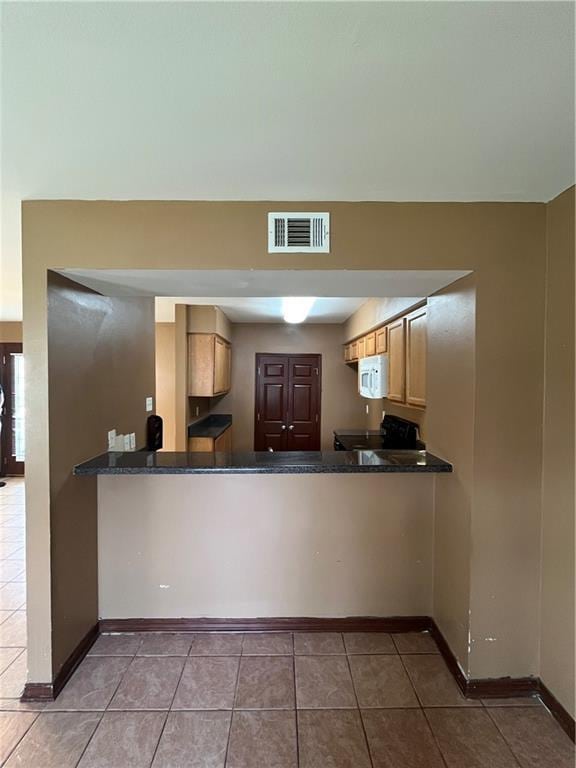 kitchen featuring visible vents, baseboards, dark countertops, white microwave, and tile patterned flooring