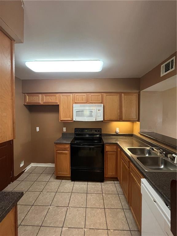 kitchen with light tile patterned floors, white appliances, a sink, visible vents, and dark countertops