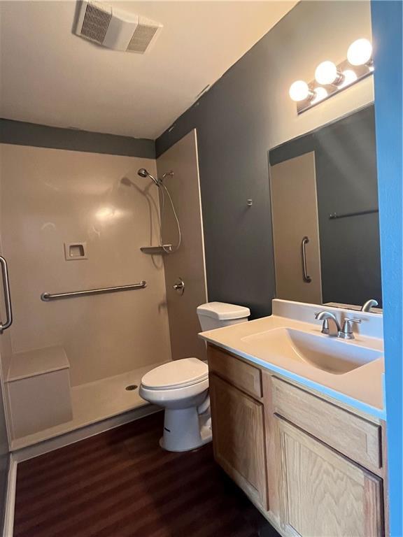 bathroom featuring a stall shower, visible vents, toilet, wood finished floors, and vanity