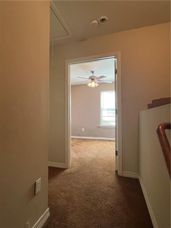 corridor featuring attic access, dark carpet, and baseboards