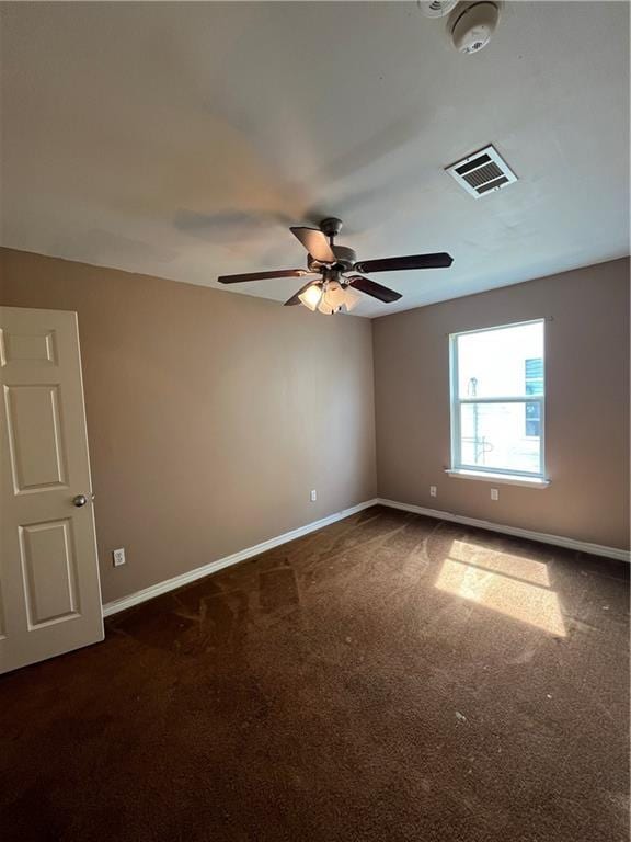 empty room featuring baseboards, visible vents, dark carpet, and a ceiling fan