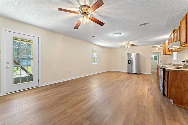 kitchen with a textured ceiling, stainless steel appliances, visible vents, light wood-type flooring, and brown cabinetry