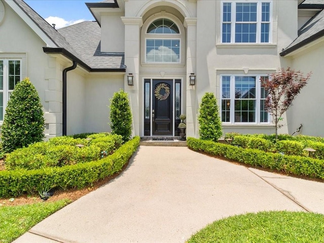 entrance to property featuring a shingled roof and stucco siding