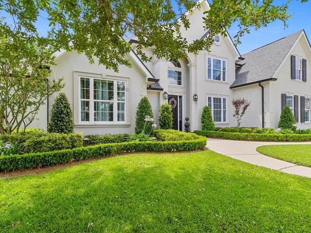 traditional home with roof with shingles, a front lawn, and stucco siding