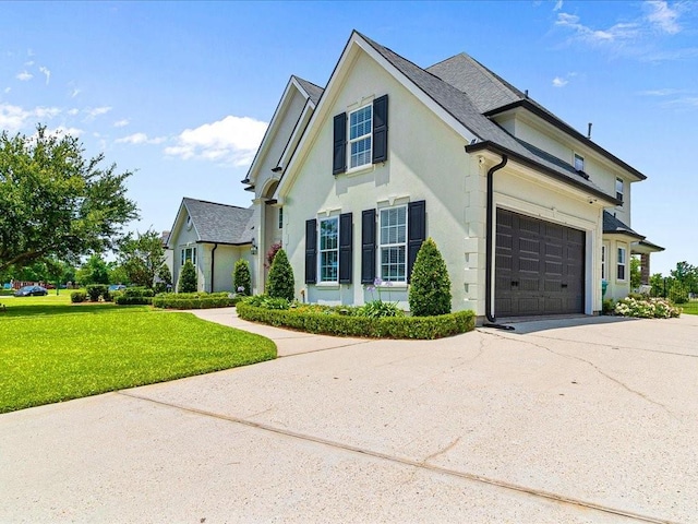 traditional-style house featuring a garage, concrete driveway, a front lawn, and stucco siding