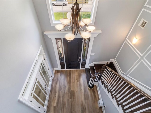 foyer featuring a notable chandelier, wood finished floors, visible vents, a towering ceiling, and stairs