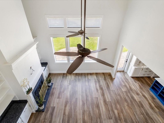 unfurnished living room featuring a fireplace, wood finished floors, a towering ceiling, and baseboards