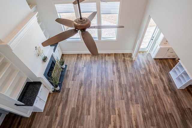 unfurnished living room featuring dark wood-style floors, ceiling fan, baseboards, and a fireplace with raised hearth