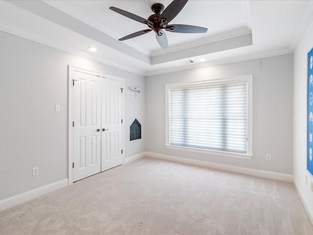 carpeted spare room featuring ceiling fan, baseboards, a raised ceiling, and crown molding