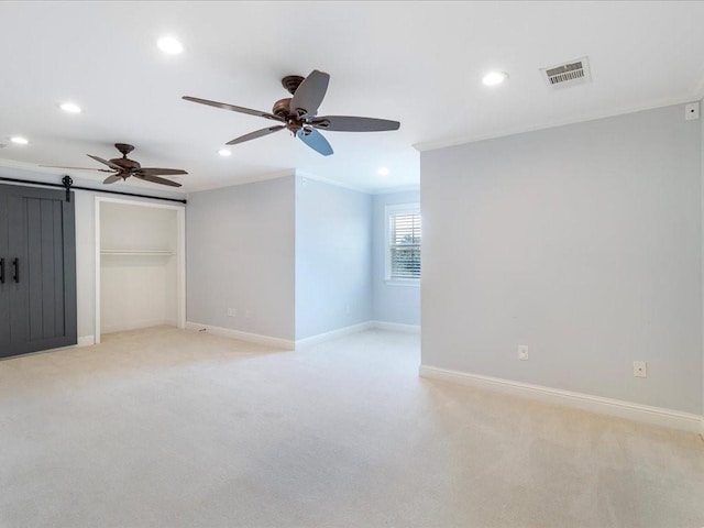 unfurnished bedroom with a barn door, baseboards, visible vents, light colored carpet, and crown molding