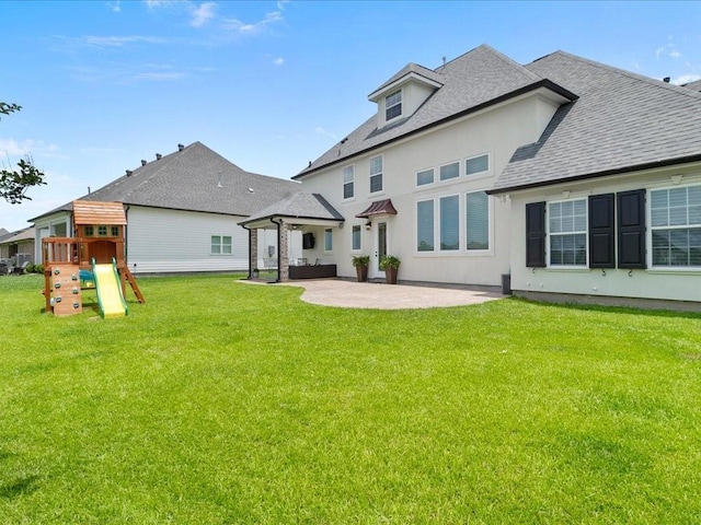 back of property featuring a playground, roof with shingles, stucco siding, a lawn, and a patio area