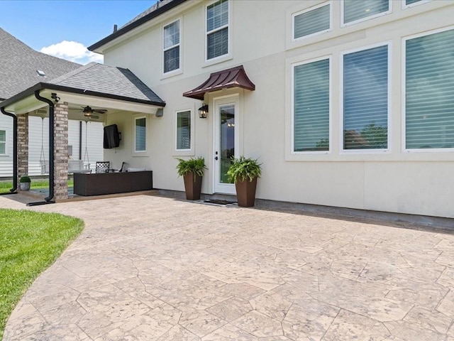 exterior space with stucco siding, a ceiling fan, a patio, and roof with shingles