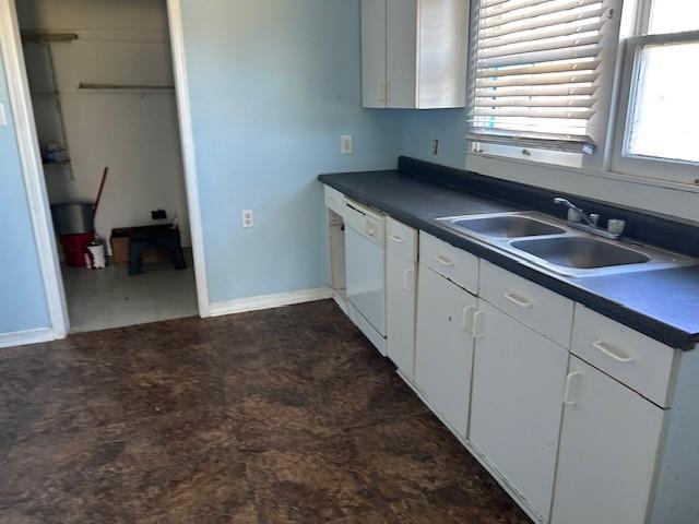 kitchen with dishwasher, dark countertops, a sink, and a wealth of natural light