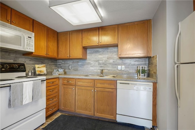 kitchen with white appliances, decorative backsplash, brown cabinets, light countertops, and a sink