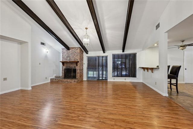 unfurnished living room with vaulted ceiling with beams, ceiling fan with notable chandelier, wood finished floors, visible vents, and a brick fireplace