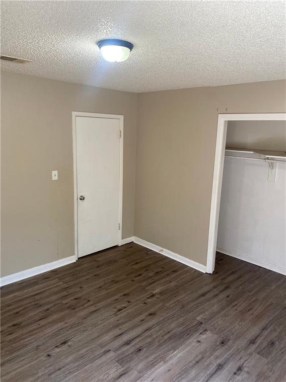 unfurnished bedroom featuring dark wood-style floors, a closet, and baseboards