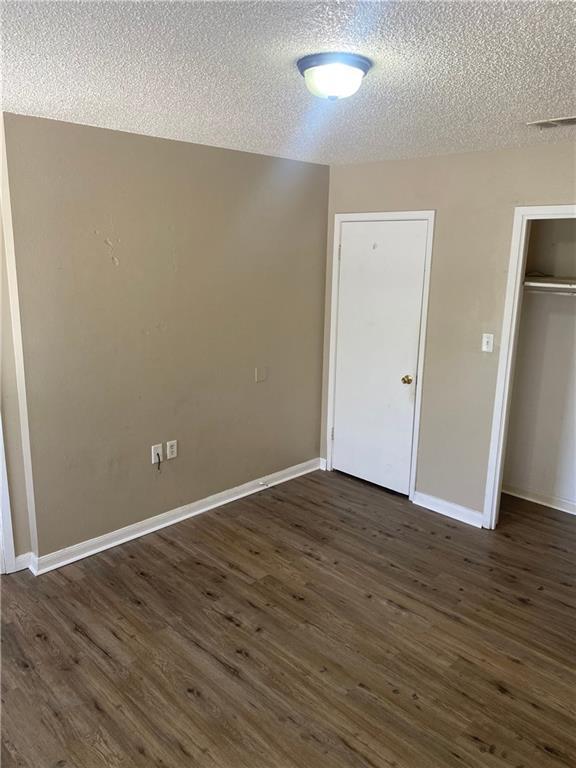 unfurnished bedroom featuring dark wood-type flooring, a closet, a textured ceiling, and baseboards