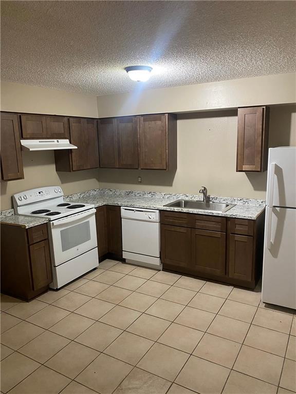 kitchen featuring white appliances, a sink, under cabinet range hood, and dark brown cabinets