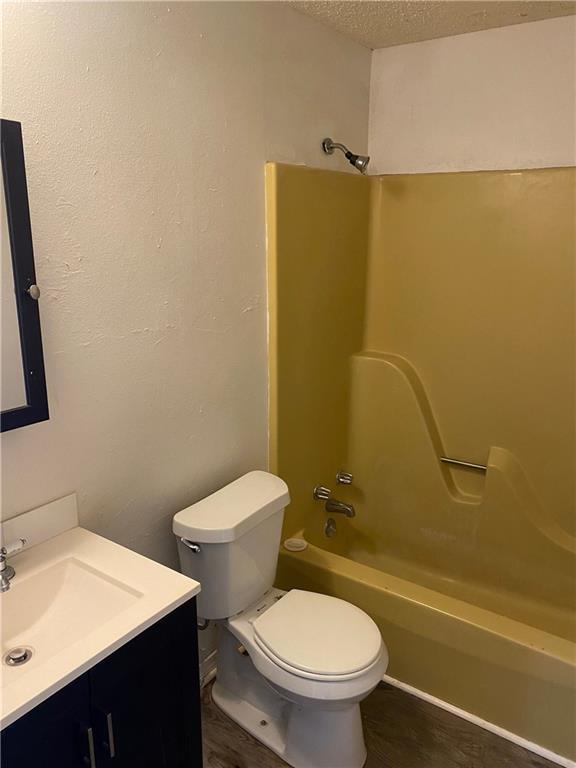 full bathroom with a textured ceiling, shower / tub combination, toilet, wood finished floors, and vanity