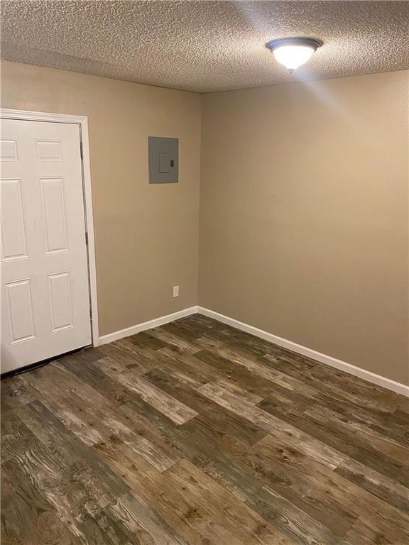 empty room featuring dark wood-style flooring, electric panel, a textured ceiling, and baseboards