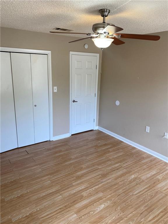 unfurnished bedroom featuring light wood-type flooring, a closet, a textured ceiling, and baseboards