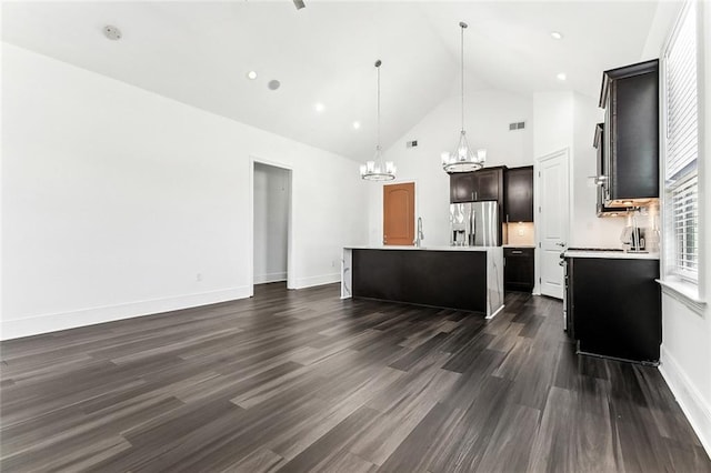 kitchen with dark wood finished floors, light countertops, an island with sink, high vaulted ceiling, and stainless steel fridge