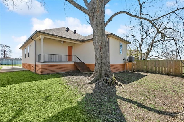 rear view of house with a yard, fence, and stucco siding