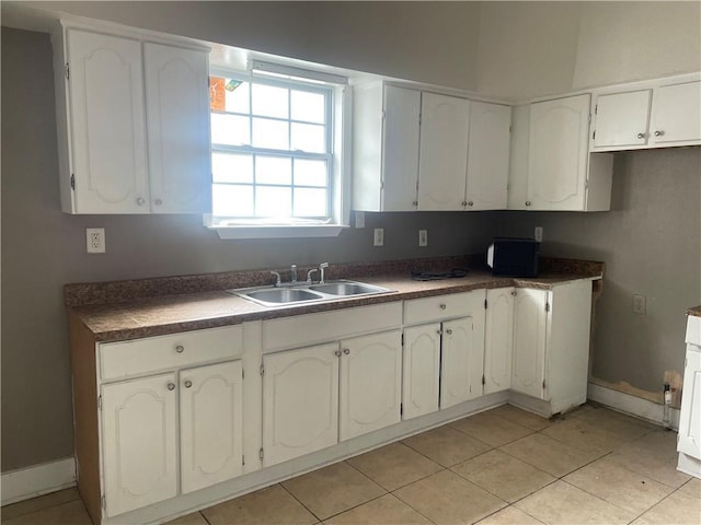 kitchen with light tile patterned flooring, white cabinetry, baseboards, and a sink