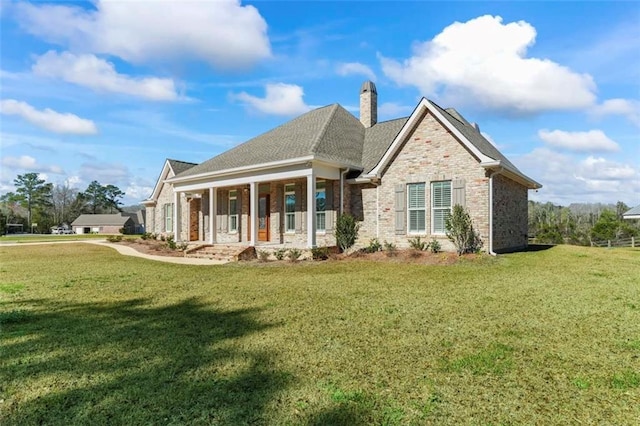 view of front of house with a shingled roof, a chimney, a front lawn, and brick siding