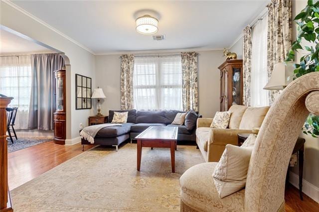 living area with arched walkways, ornamental molding, plenty of natural light, and wood finished floors